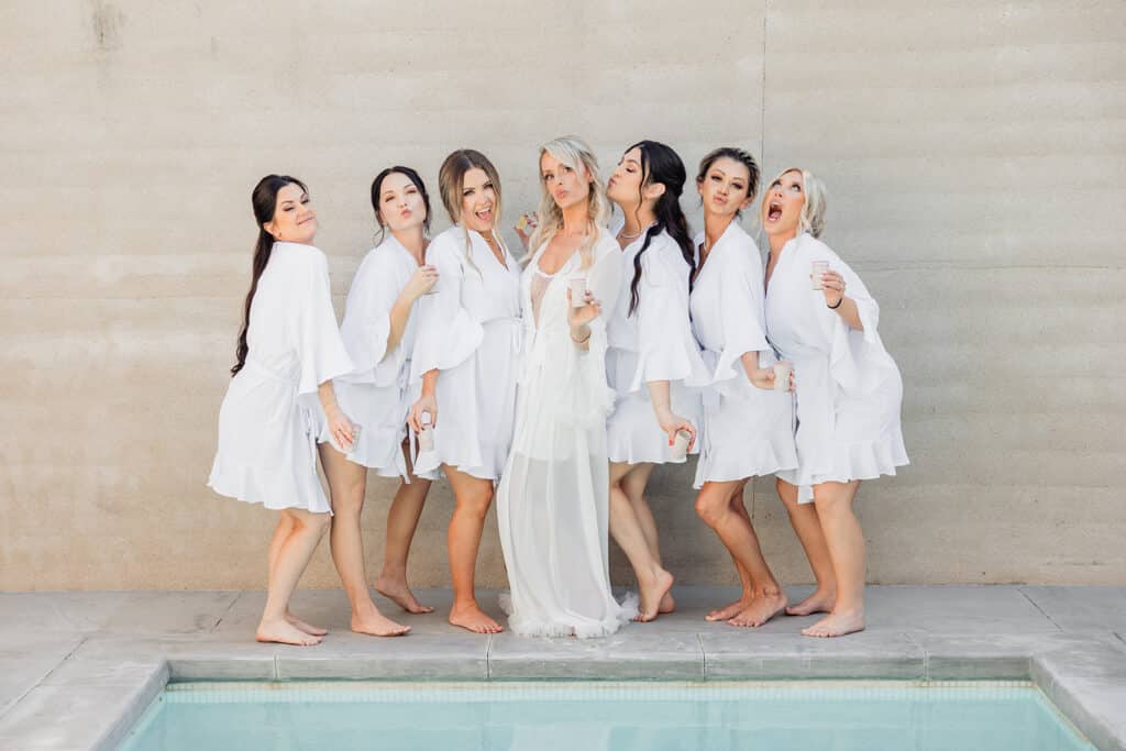 Bride and bridesmaids taking fun photos before wedding in matching white robes. Cabo destination wedding.
