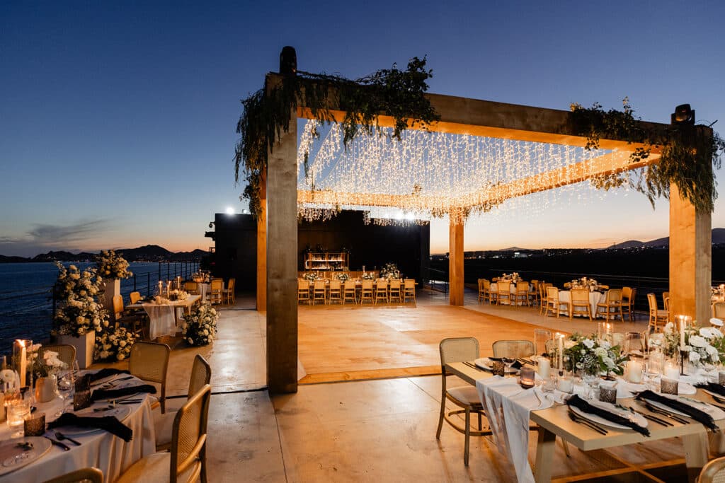 Cabo wedding at the Cape rooftop, in neutral tones using lighting, long tables and rounds with linens. wood, ivory, white and greenery wedding.
