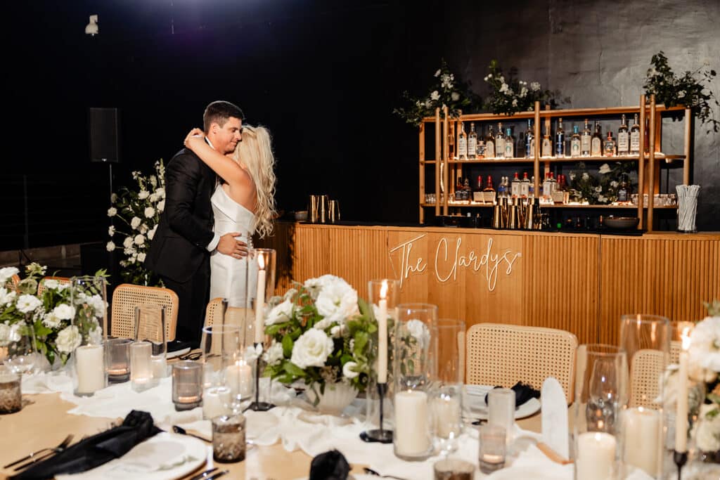 Couple sees their wedding reception for the first time. They hug and cry. They loved the decor, the details on the tables, the beautiful wooden bar with their lastname in a neon sign and the cascade of fairy lights over the dancefloor.