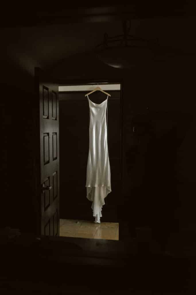 Elegant satin wedding dress hanging in a doorway before Christine and Alex's destination wedding in Los Cabos.