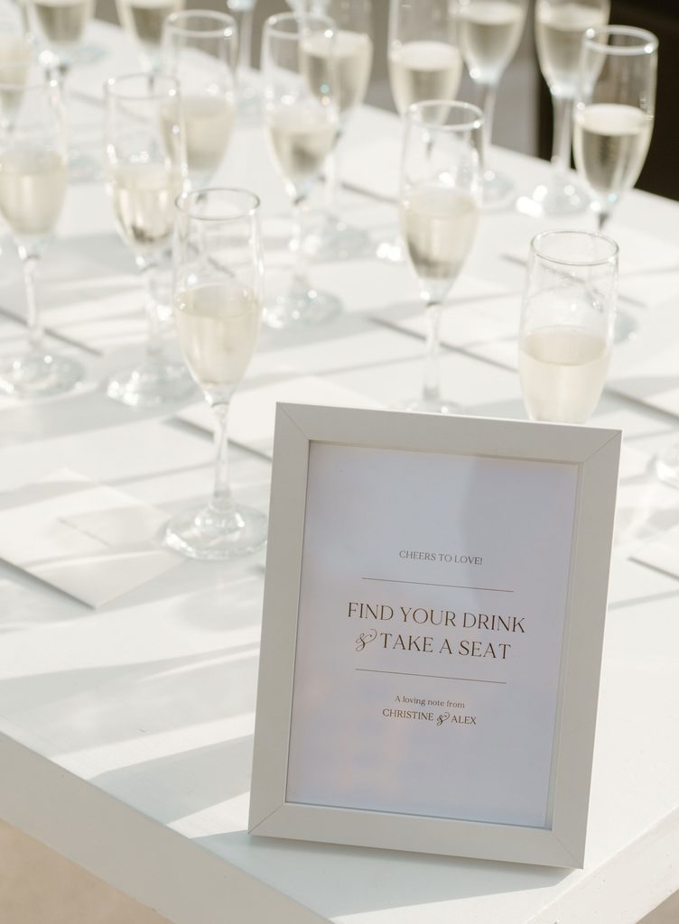 Champagne glasses and a framed seating sign inviting guests to find their drink and seat at a Cabo wedding.