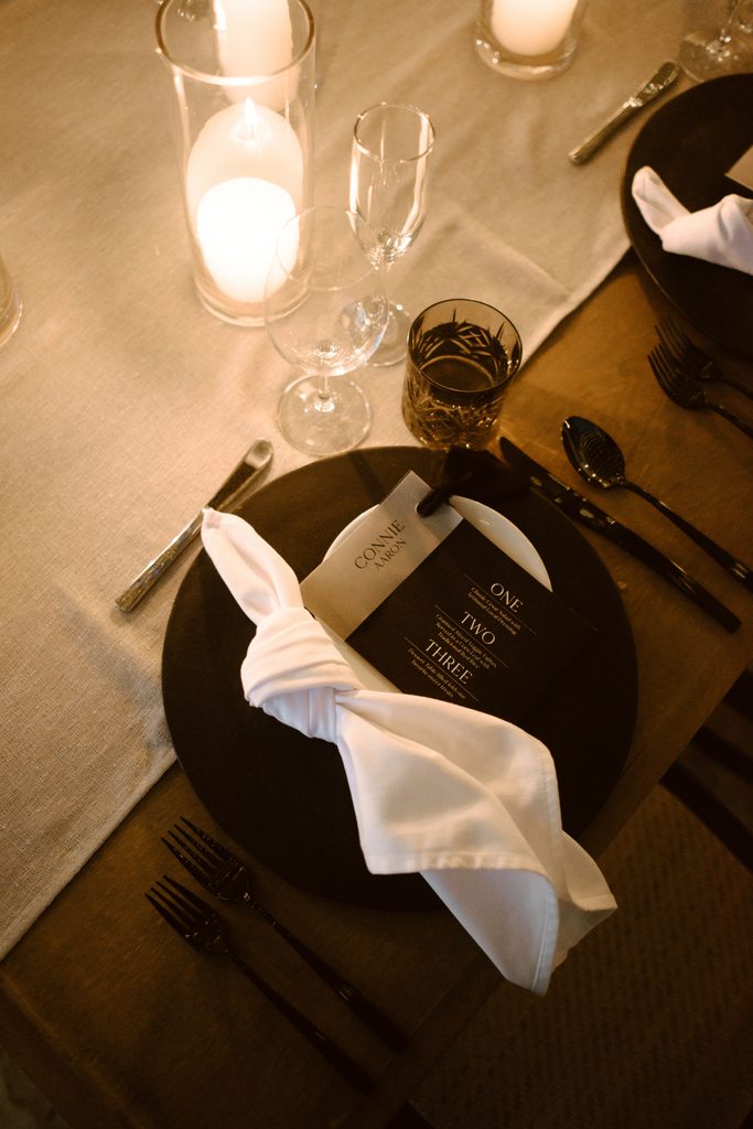 Elegant black-and-white wedding place setting with a personalized name tag and candlelight